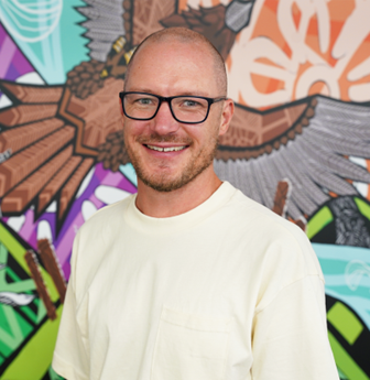 Man with glasses smiling in front of colourful mural background